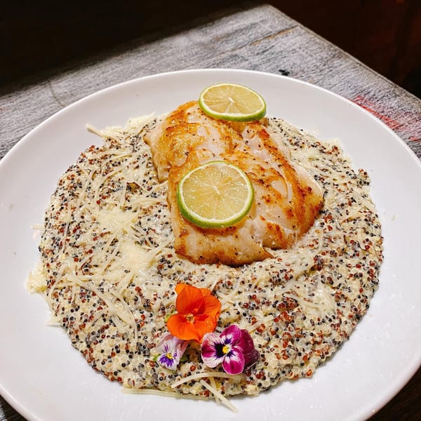 Pan-seared fish with lime slices, served over quinoa risotto with edible flowers.