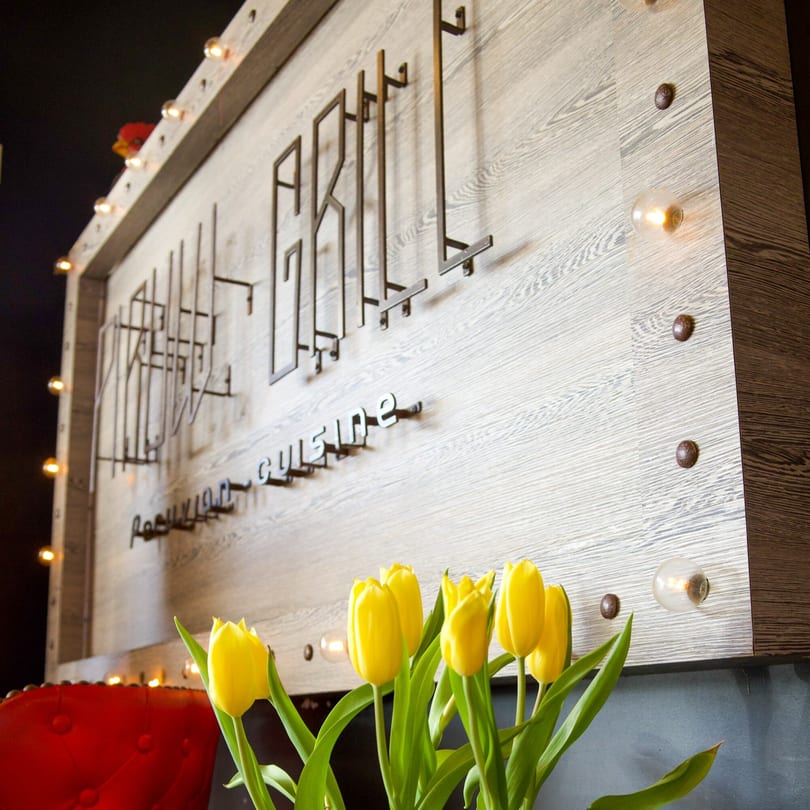 Yellow tulips in front of a wooden sign with "Grill" and "Restaurant Cuisine" in metal letters.