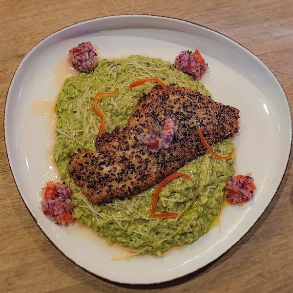 Quinoa-crusted fish over green risotto, garnished with red pepper strips and salsa on a white plate.
