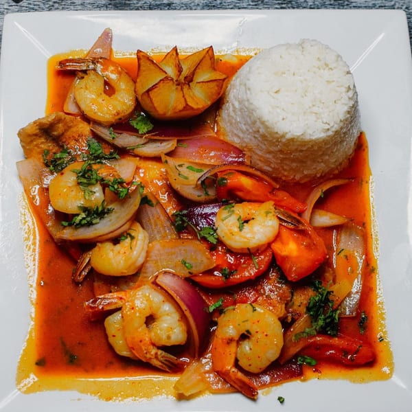 Shrimp and vegetables in a rich red sauce, with a side of white rice and a fried plantain.