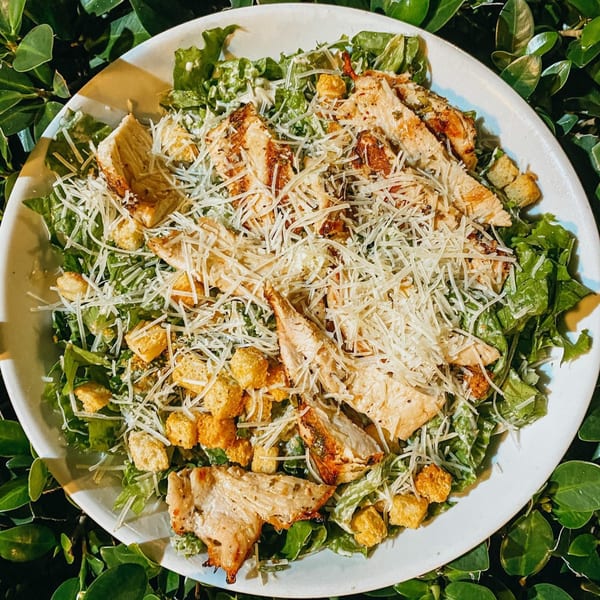Chicken Caesar salad with grilled chicken, croutons, and shredded Parmesan cheese on a white plate.