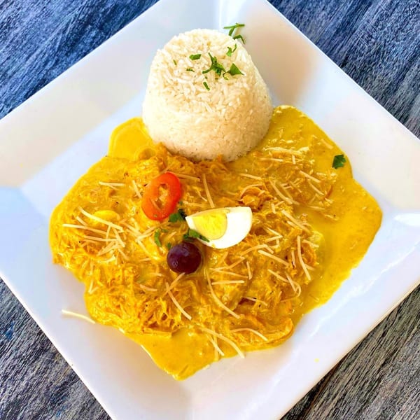 Aji de Gallina, a Peruvian dish with shredded chicken in yellow sauce, rice, egg, and olive.