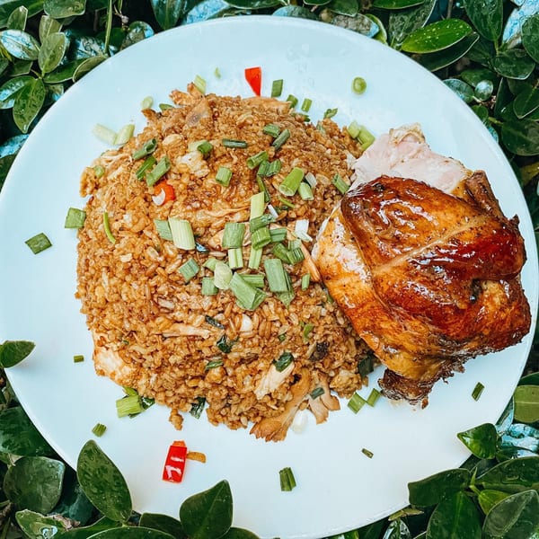 A plate of golden brown fried rice with chopped scallions and a roasted chicken quarter.